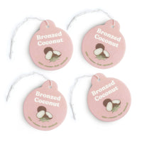 Four pink round car charms with "Bronzed Coconut" text, coconut illustrations, and scent descriptors, each with a white strin