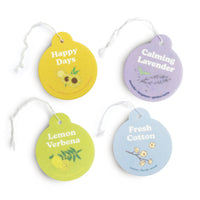 Four round car air freshener charms in yellow, lime green, lavender, and light blue with floral designs and white string atta
