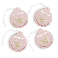 Four pink round car charms with "Florence" text, floral illustrations, and scent descriptions with attached string loops.