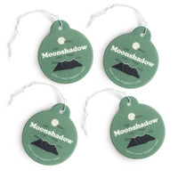 Four green round car charms with white string loops, each featuring "Moonshadow" text and a black mountain silhouette design.