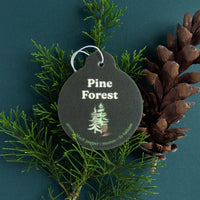 Dark gray round car charm with white metal loop, displaying "Pine Forest" text and tree illustration, surrounded by fresh pin