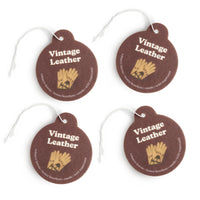 Four brown leather round charms with gold wheat design, white text, and white string attachments.