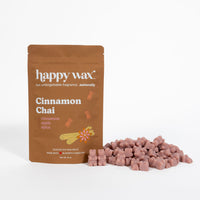 Brown pouch of Happy Wax Cinnamon Chai wax melts with scattered dusty rose-colored wax cubes displayed in front.