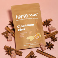 Tan pouch of cinnamon chai scented soy wax melts surrounded by star anise, cinnamon sticks, and small wax pieces on pink back