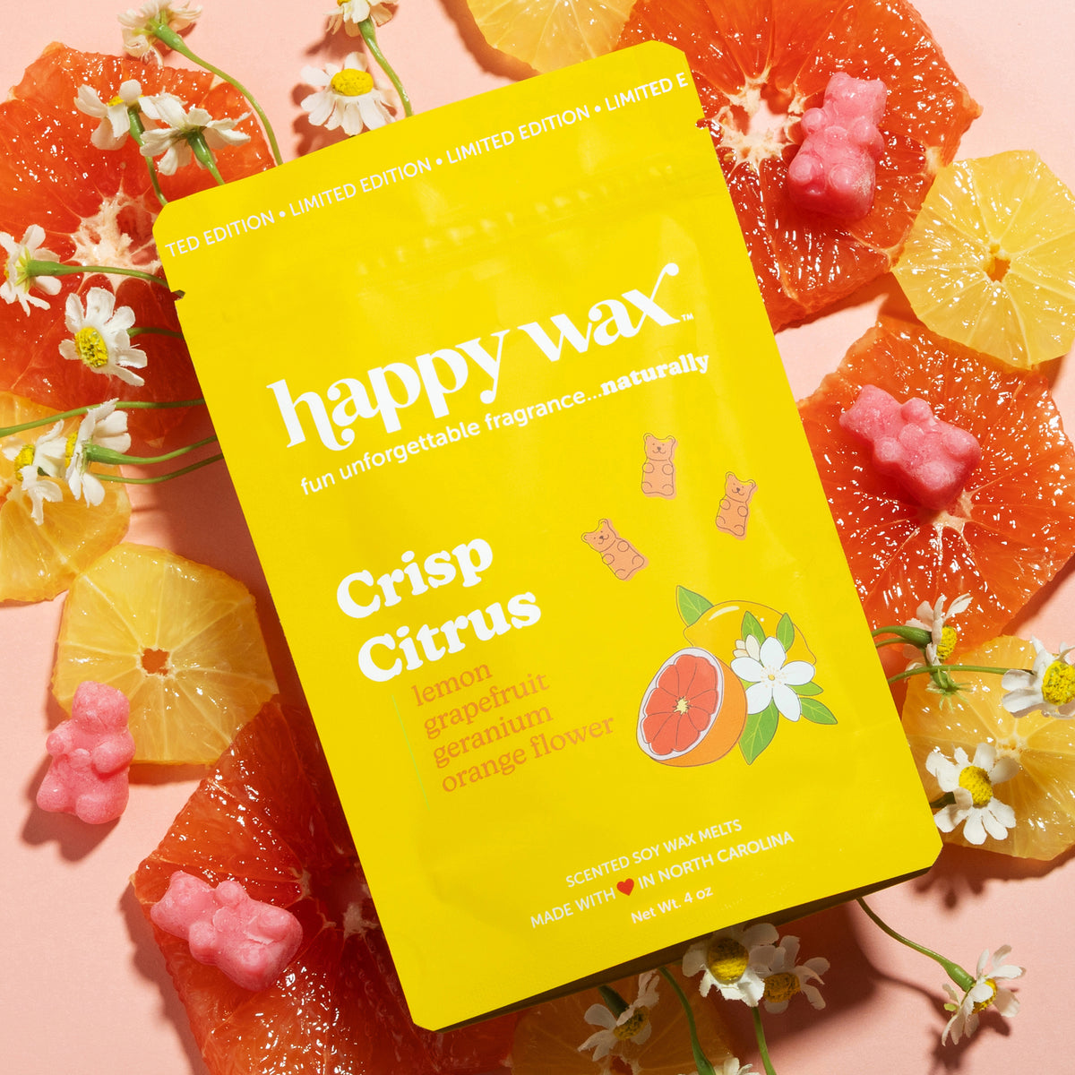 Happy Wax Crisp Citrus wax melt packaging surrounded by sliced lemons and grapefruit with flowers on a peach background