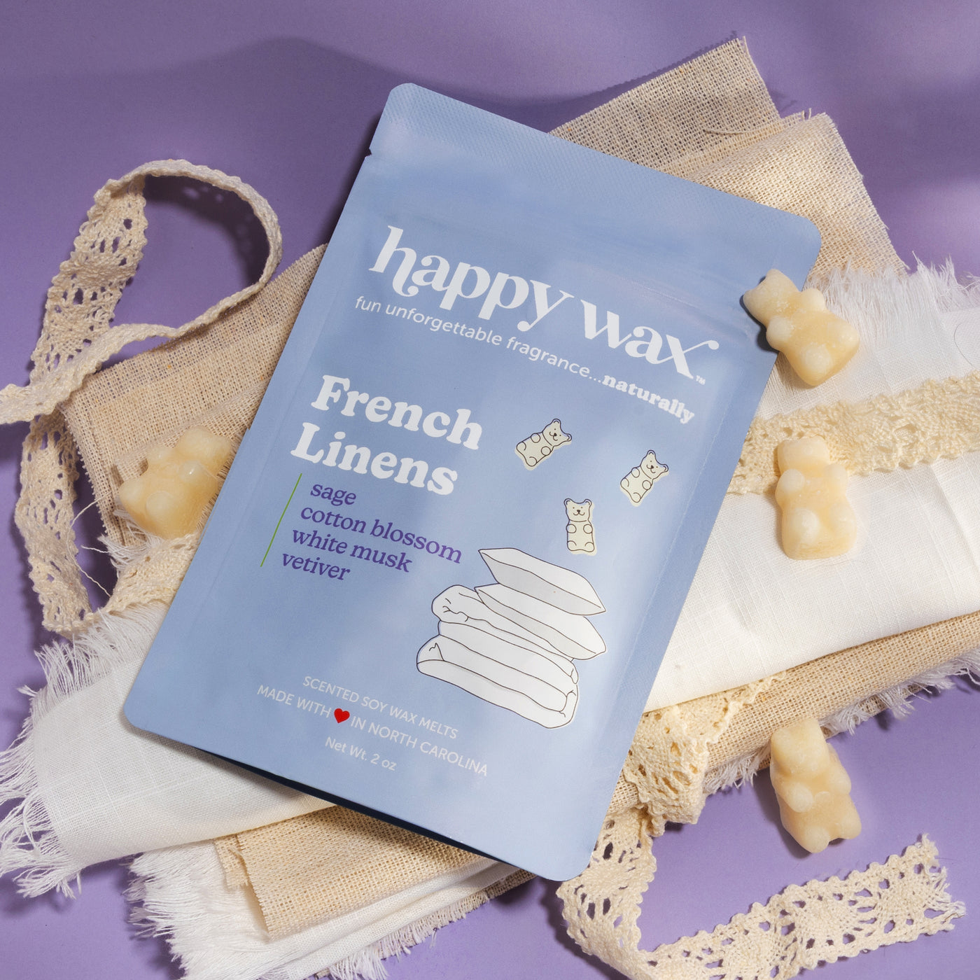 Happy Wax French Linens packaging with linen fabric and ribbon on purple background