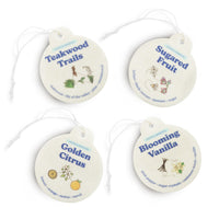 Four cream-colored round car charms with string attachments labeled Teakwood Trails, Sugared Fruit, Golden Citrus, and Bloomi