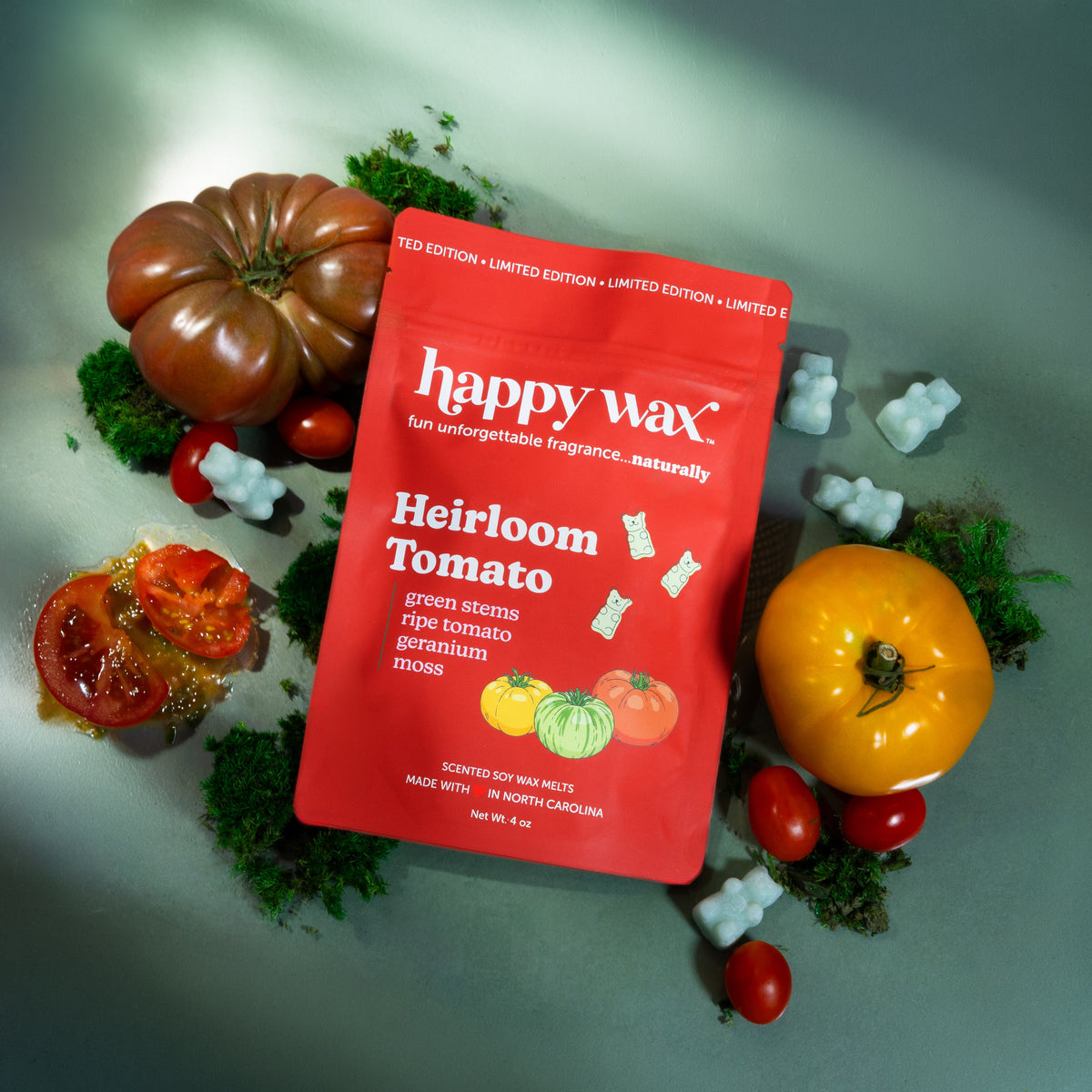 happy wax Heirloom Tomato wax melt packaging surrounded by decorative tomatoes and plants on a green background