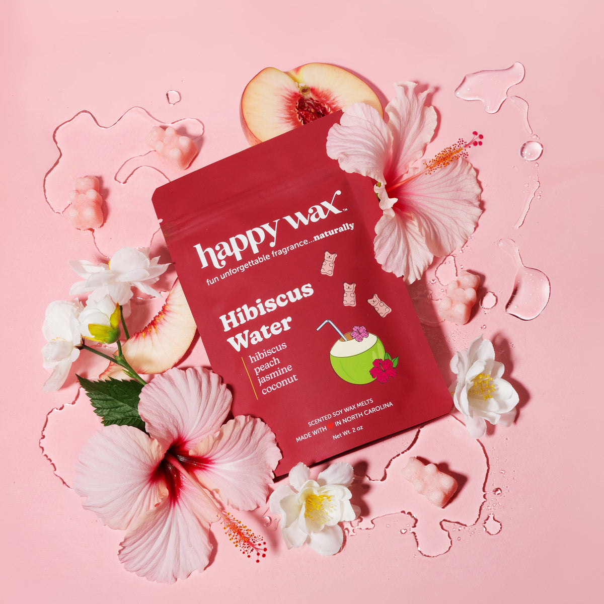 Red 'happy wax' Hibiscus Water packaging surrounded by flowers on a pink background