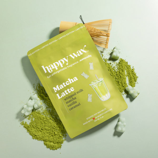 Lime green wax melt package labeled "Matcha Latte" with matcha powder, wax chunks, and a whisk brush on pale green background