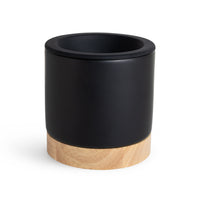 Black cylindrical wax warmer with natural wood base and open top chamber.