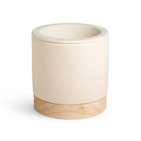 Cream ceramic wax warmer with natural wood base and open top bowl.