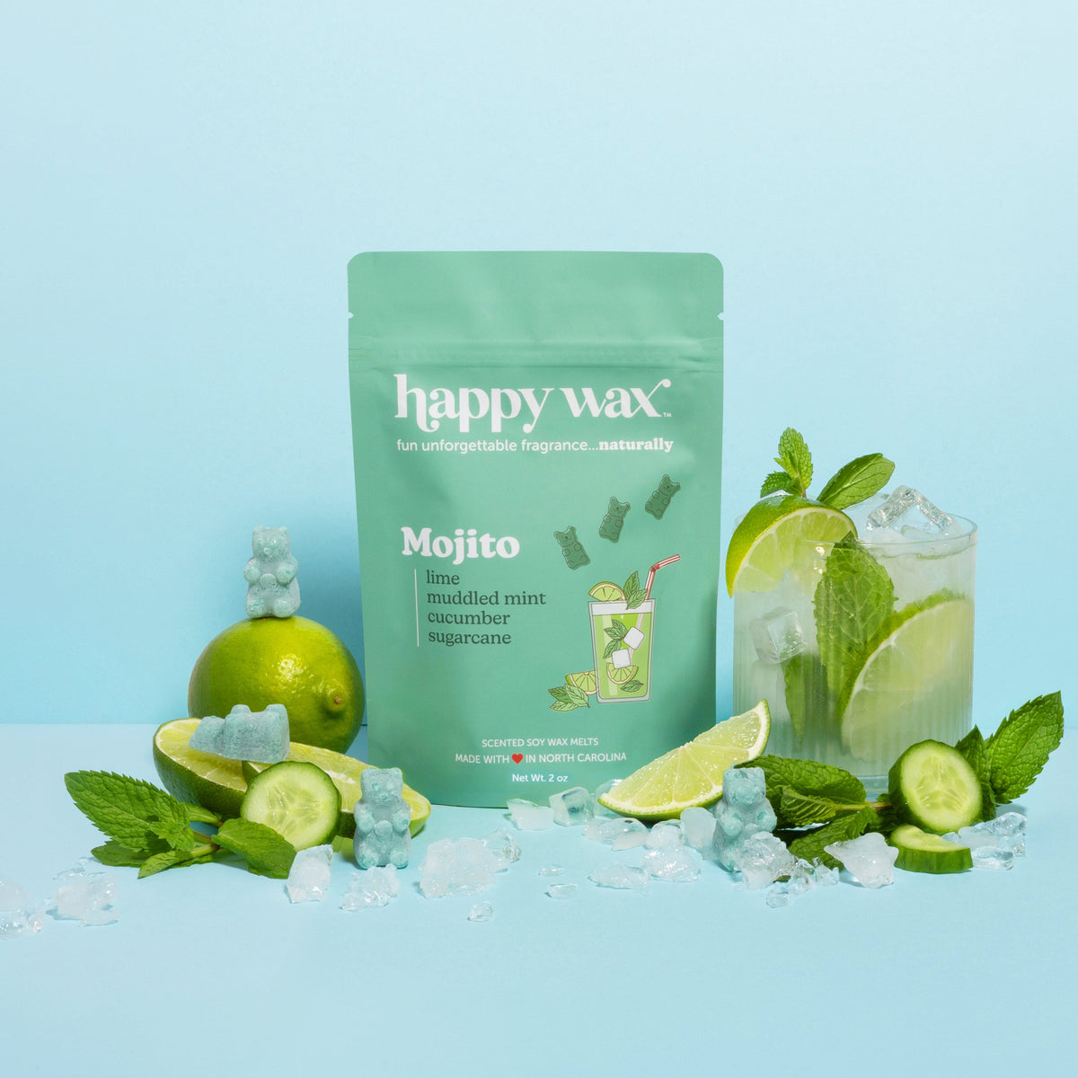 Happy Wax Mojito packaging and cocktail with lime slices and mint leaf accent with wax melts, limes, mint leaves, and crushed ice scattered on a light blue background