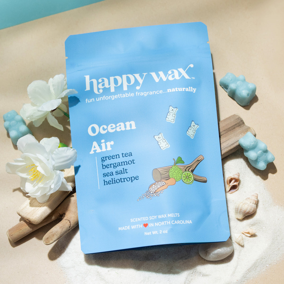 Happy Wax Ocean Air wax melts packaging on a sandy background with beach wood and white flowers.