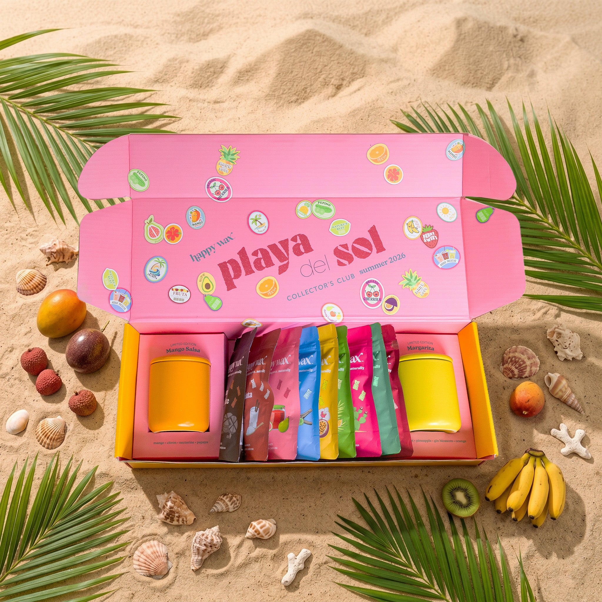 Pink 'playa del sol' subscription box on sand with tropical fruits and leaves