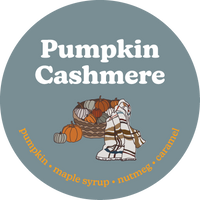 Round gray-blue label with white text reading "Pumpkin Cashmere" and illustrations of pumpkins and a plaid blanket.