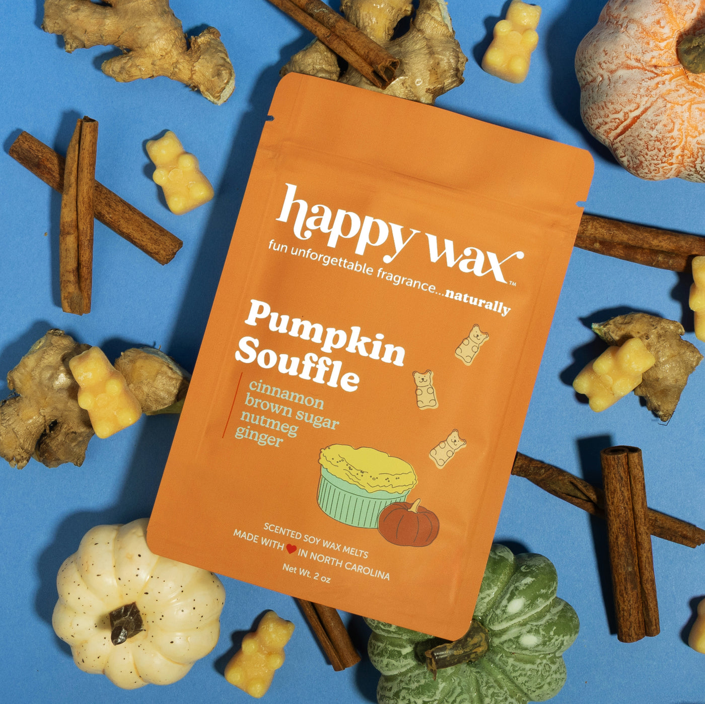 Happy Wax Pumpkin Souffle Pouch with pumpkins, ginger root, and cinnamon sticks on blue background