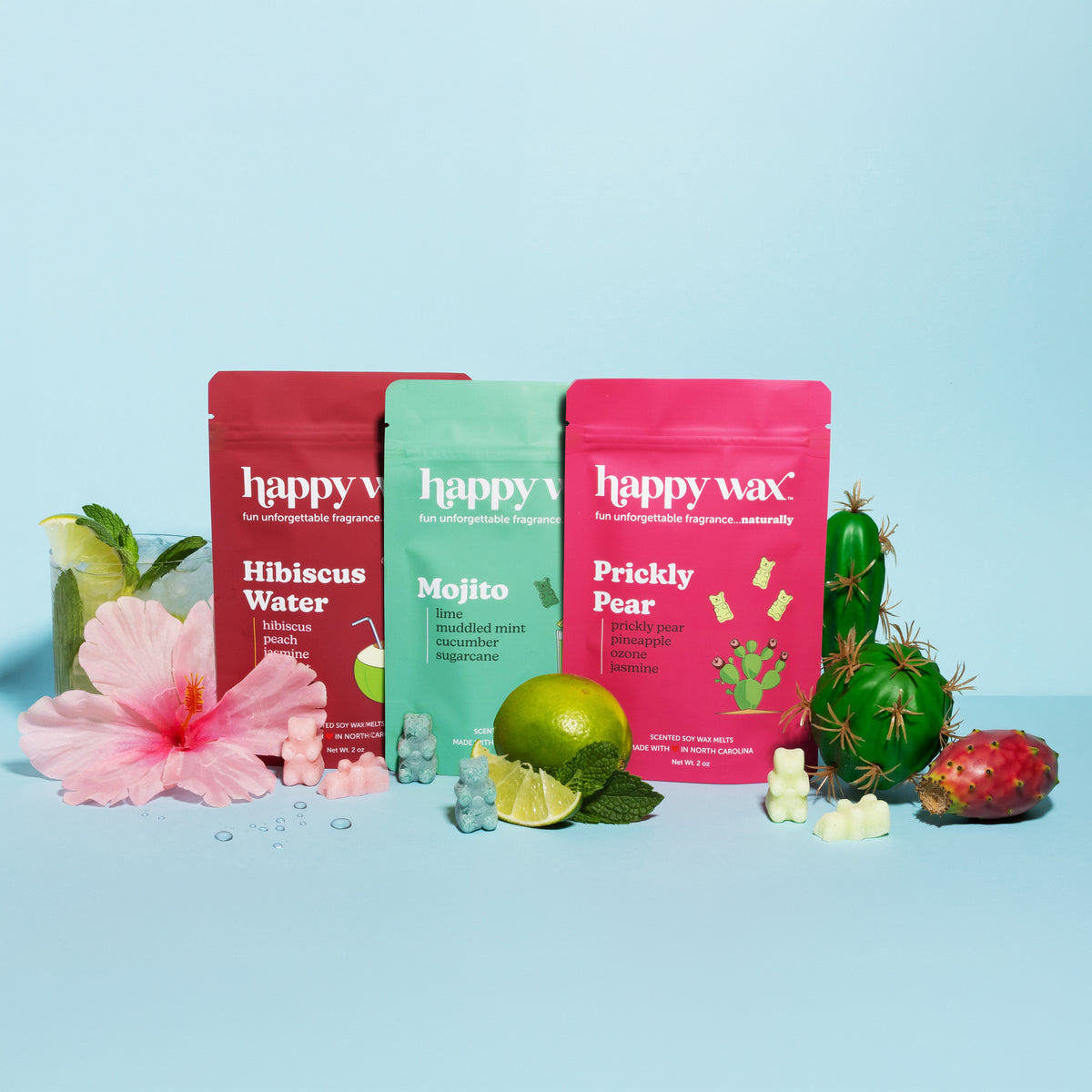 Three 'happy wax' wax melt packages with tropical limes, hibiscus, and prickly pears on a blue background