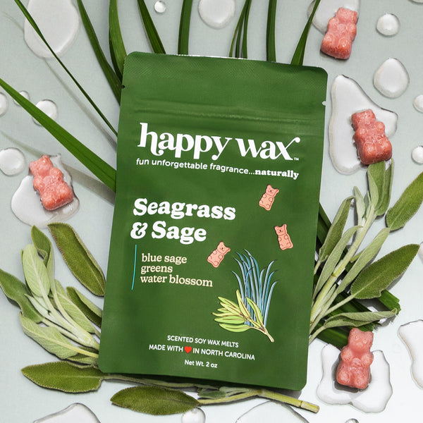 Green pouch of Happy Wax Seagrass & Sage wax melts surrounded by coral-colored wax melts, white tea light holders, and fresh