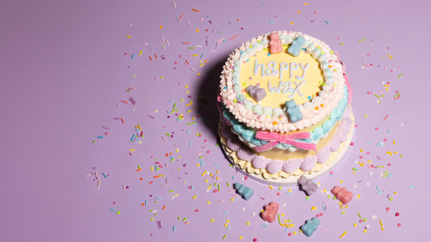 birthday cake with 'happy wax' written on it, with sprinkles, and wax bears on a purple background