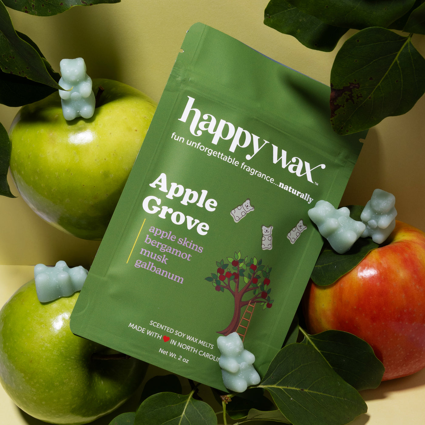 Green happy wax package surrounded by white wax melts, fresh apples, and green leaves on yellow background.