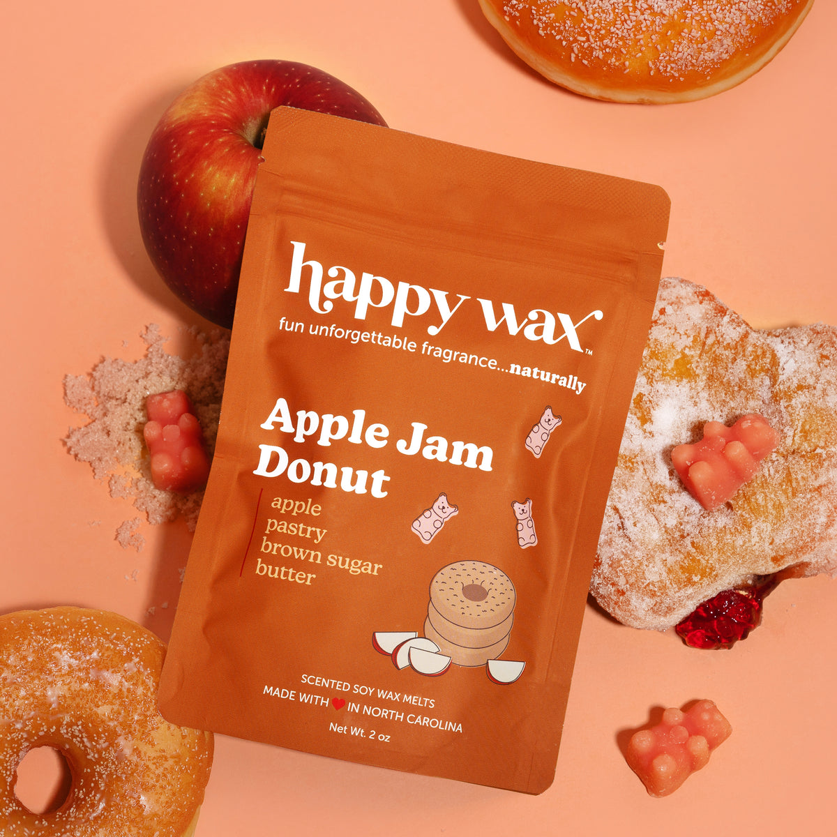 Orange Happy Wax pouch with Apple Jam Donut label surrounded by a red apple, sugar-coated donut, and red jam pieces on peach 