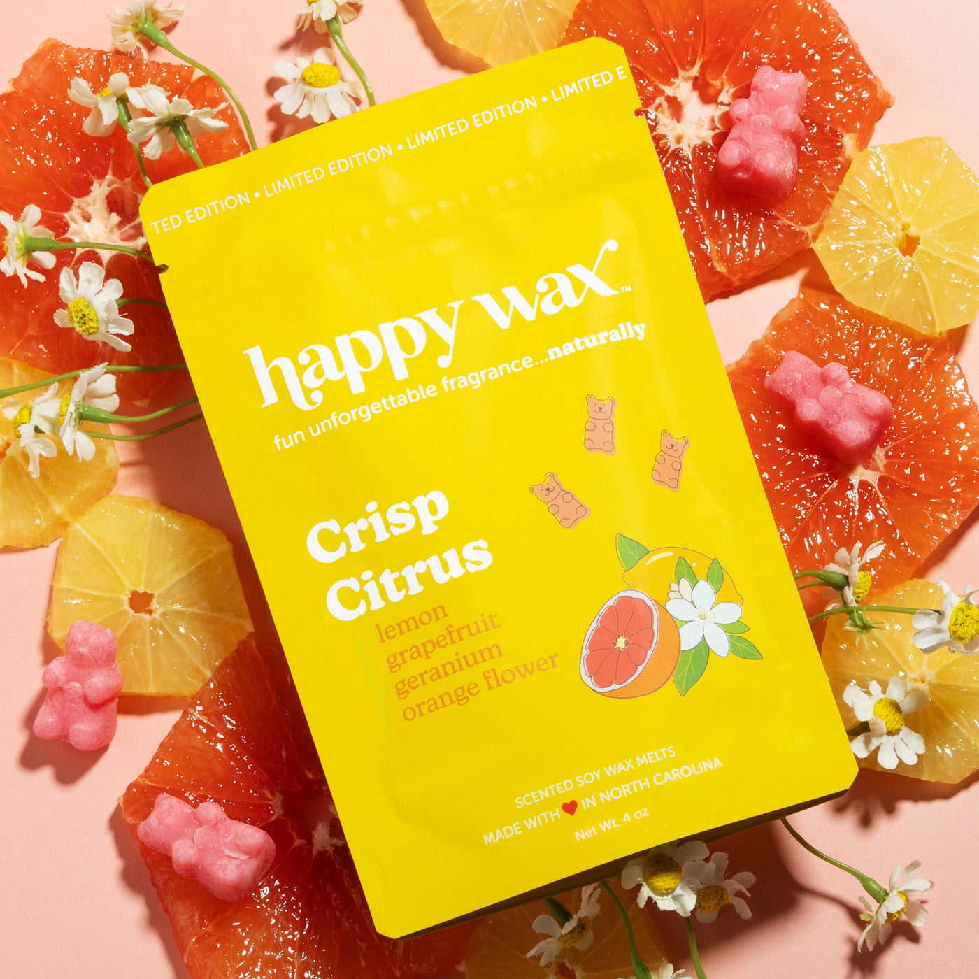 Happy Wax Crisp Citrus wax melt packaging surrounded by sliced lemons and grapefruit with flowers on a peach background