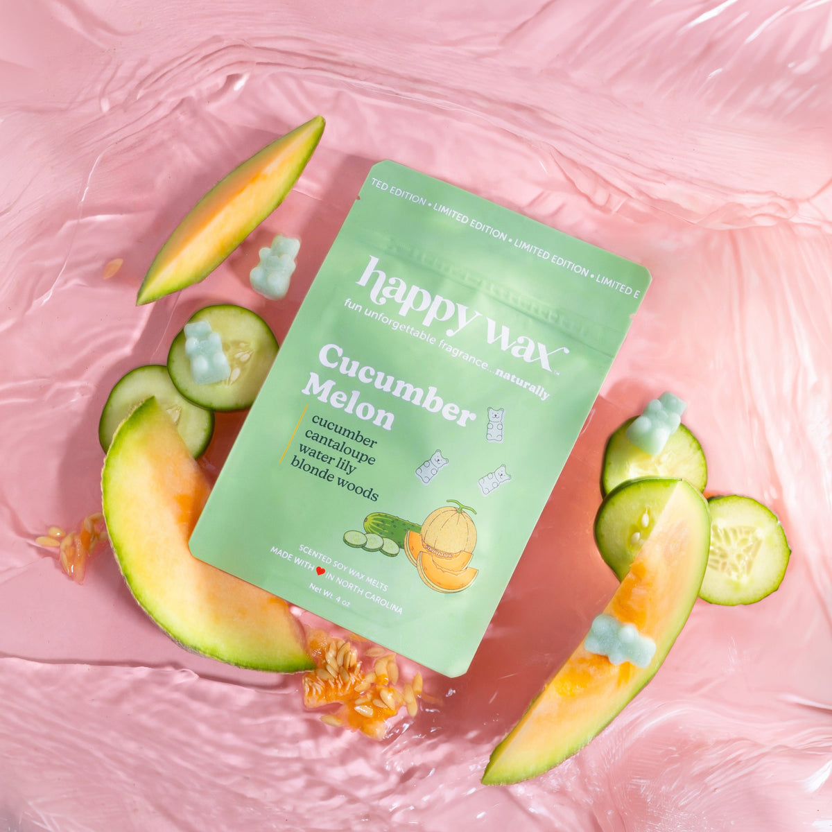 Happy Wax Cucumber Melon wax melt package on a pink background with sliced melon and cucumbers.