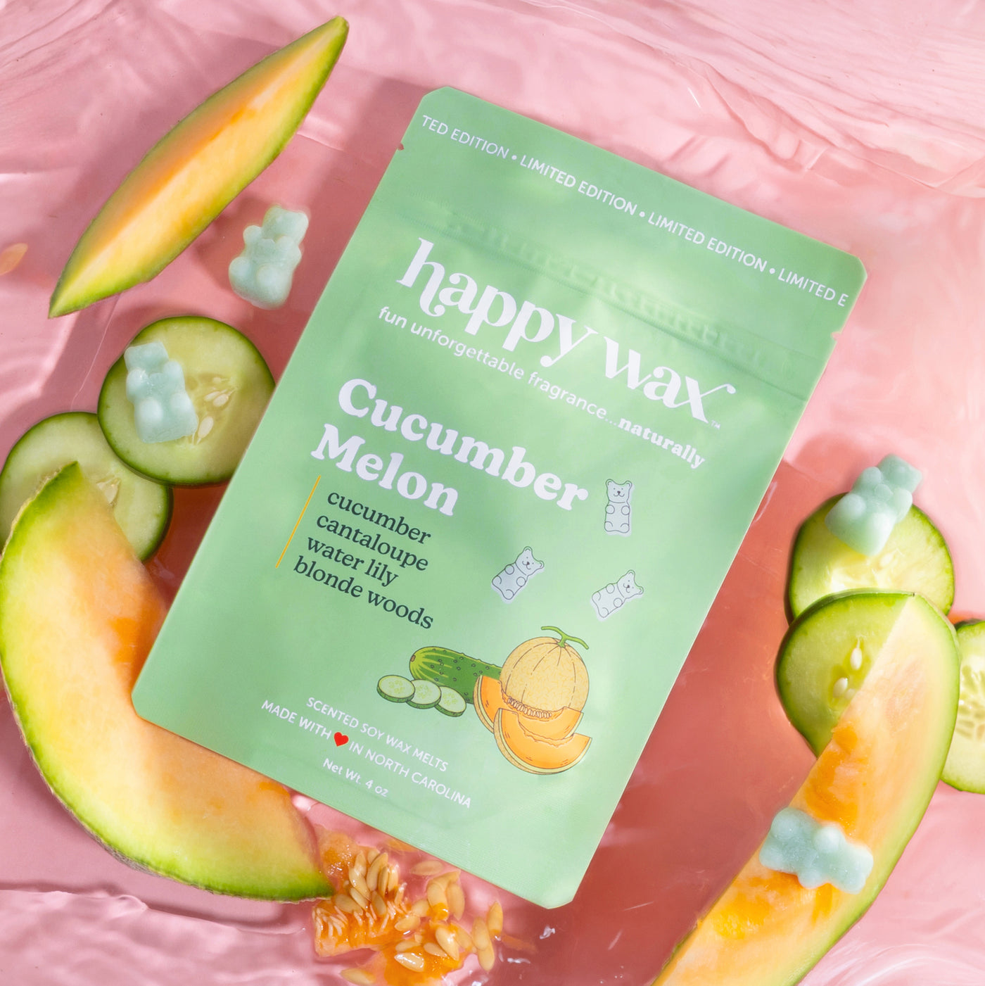 Happy Wax Cucumber Melon wax melt package on a pink background with sliced melon and cucumbers.