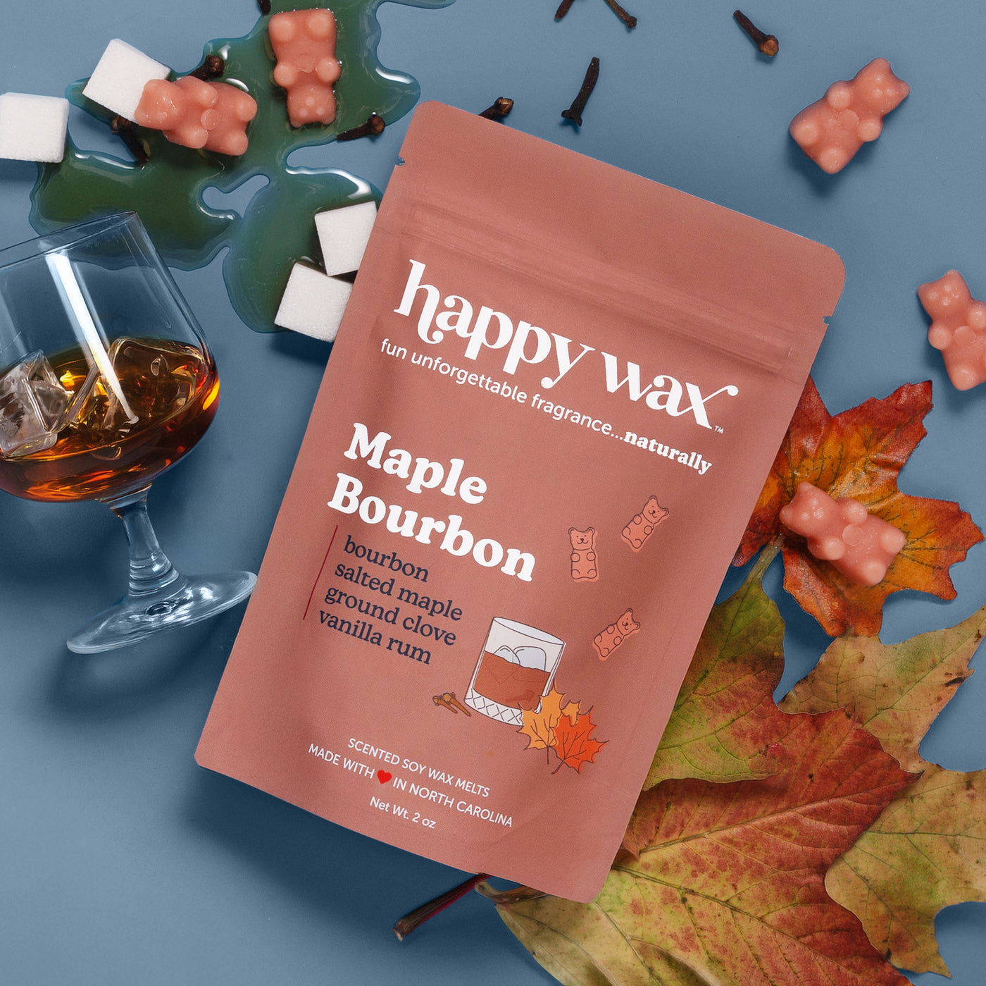 Happywax Maple Bourbon wax melt pouch surrounded by coral-colored wax melts, autumn leaves, bourbon glass, and green dish on 
