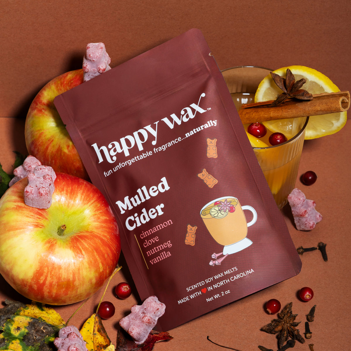 happy wax mulled cider pouch with cider, apples, fall spices, and fall leaves on brown background