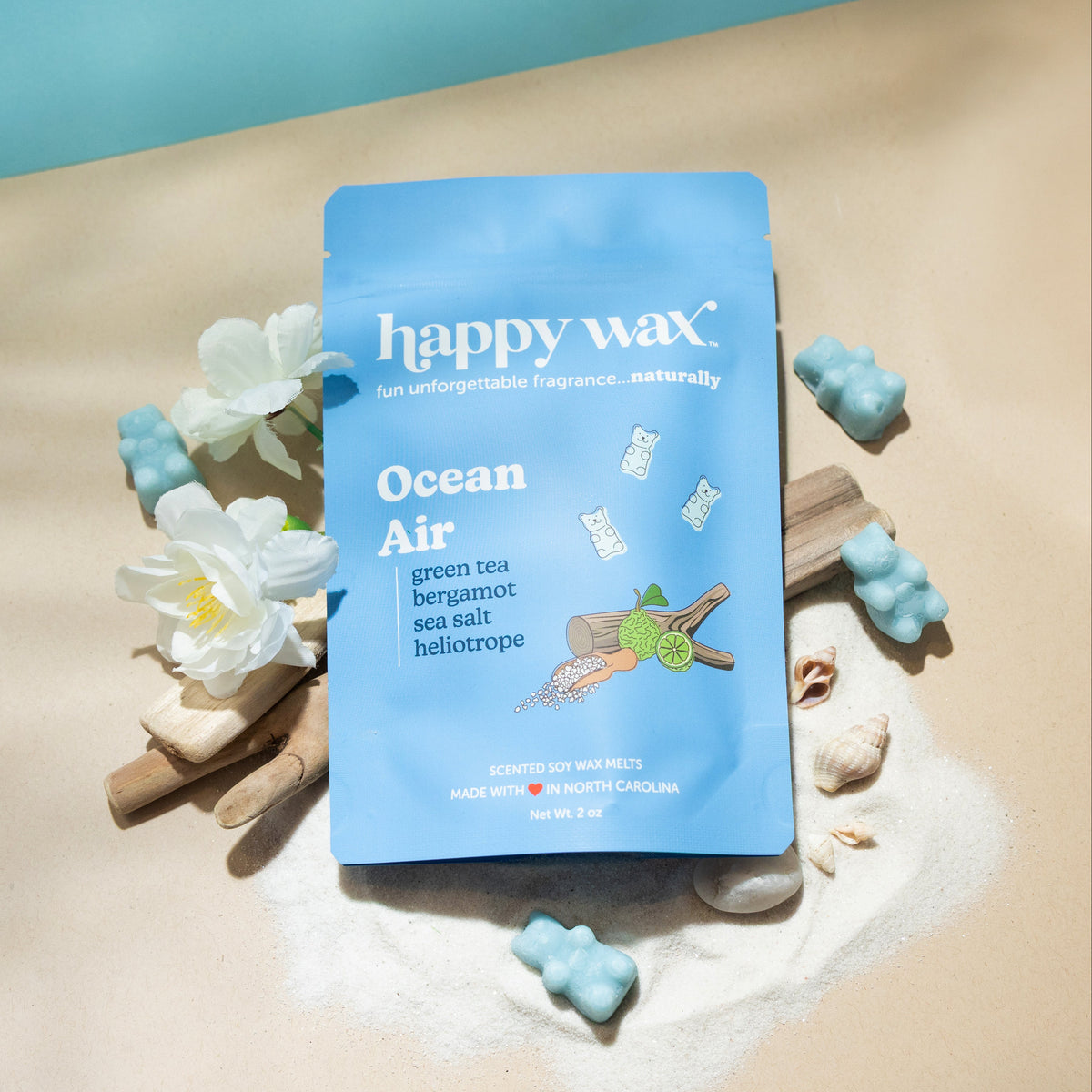 Happy Wax Ocean Air wax melts packaging on a sandy background with beach wood and white flowers.