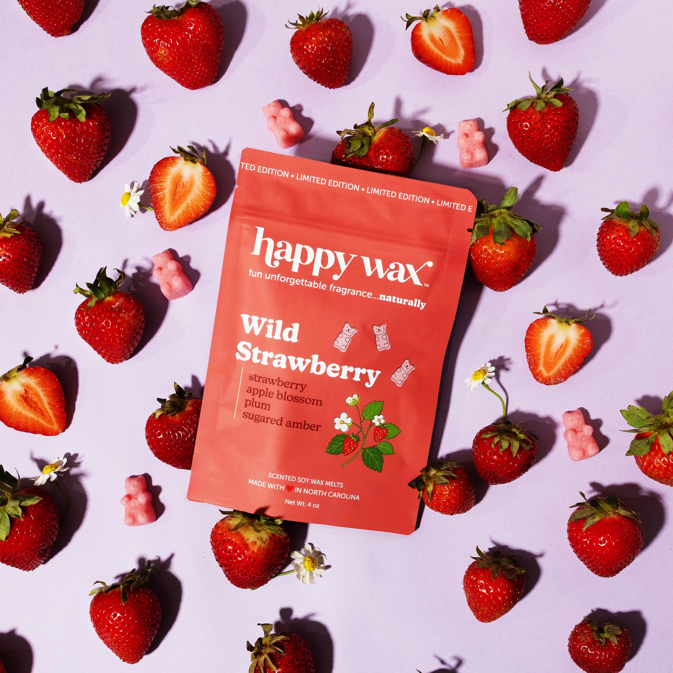 happy wax Wild Strawberry wax melt packaging surrounded by strawberries on a light purple background
