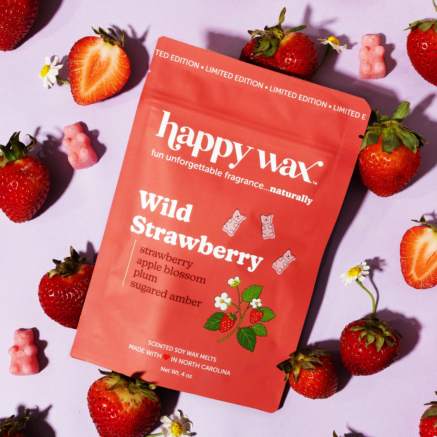 happy wax Wild Strawberry wax melt packaging surrounded by strawberries on a light purple background